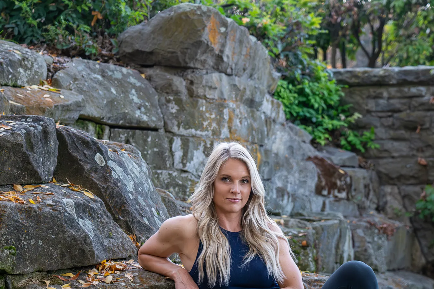 Meghan Melin seated on a moss-covered rock wall by a stream, looking off-camera
